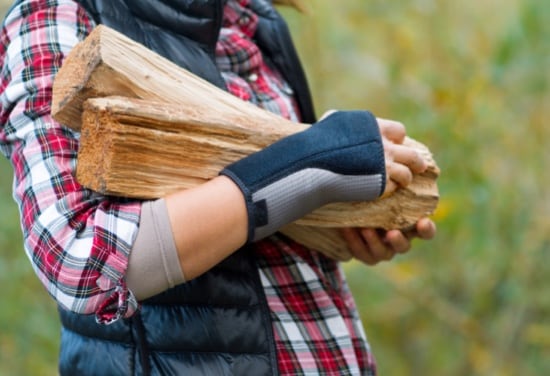 A woman wearing a wrist support, carrying two logs.
